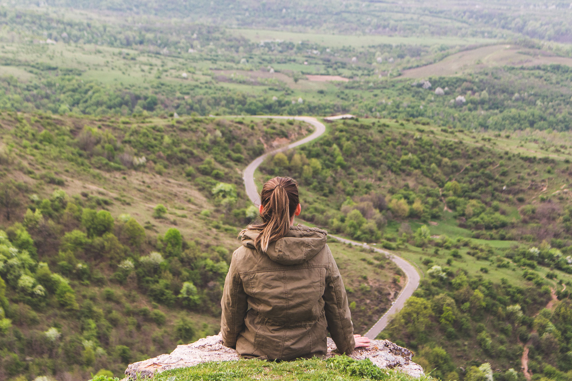 girl sitting looking out at long winding road ahead